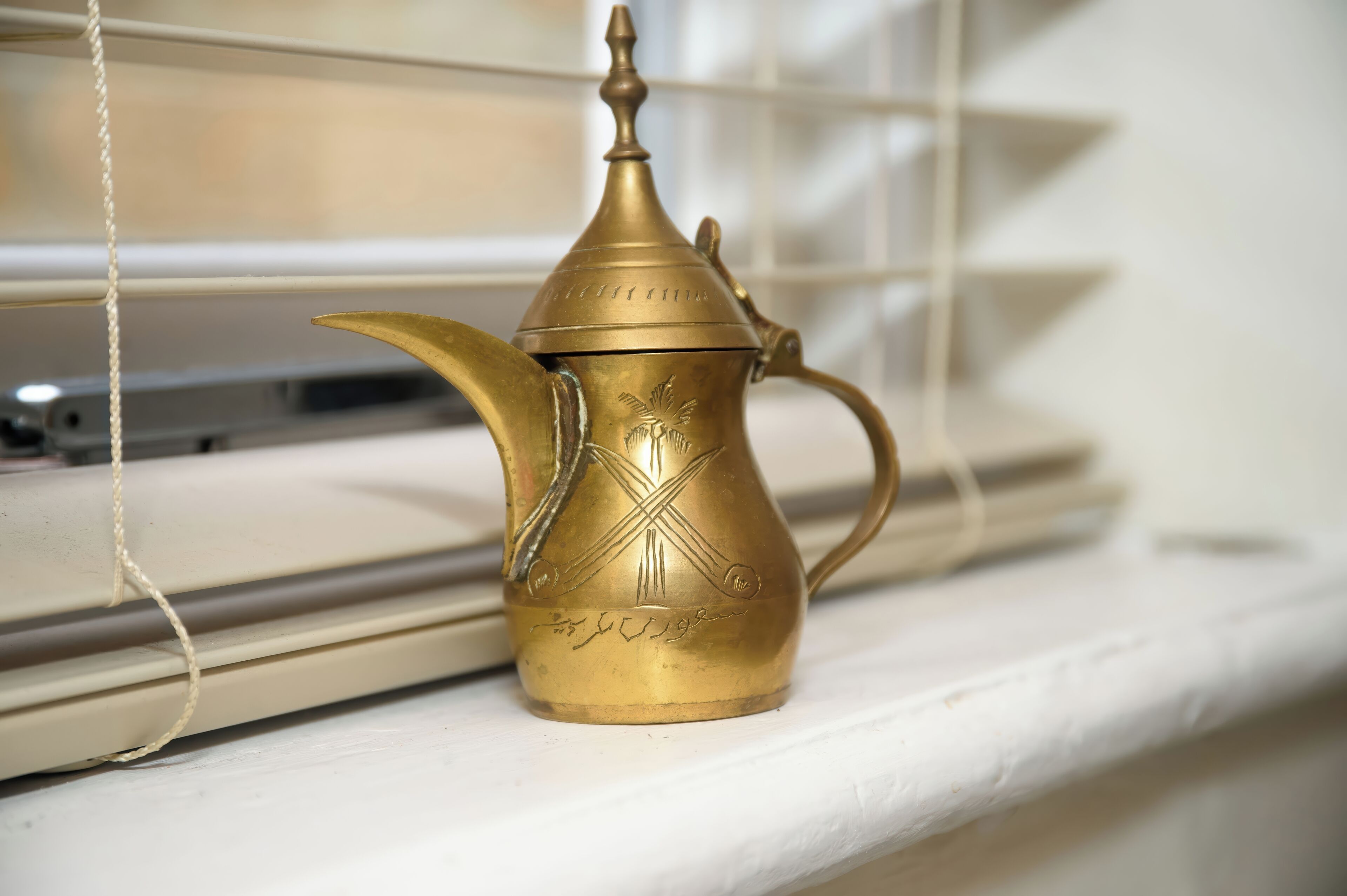 Una tetera de bronce con diseños intrincados sobre un alféizar.