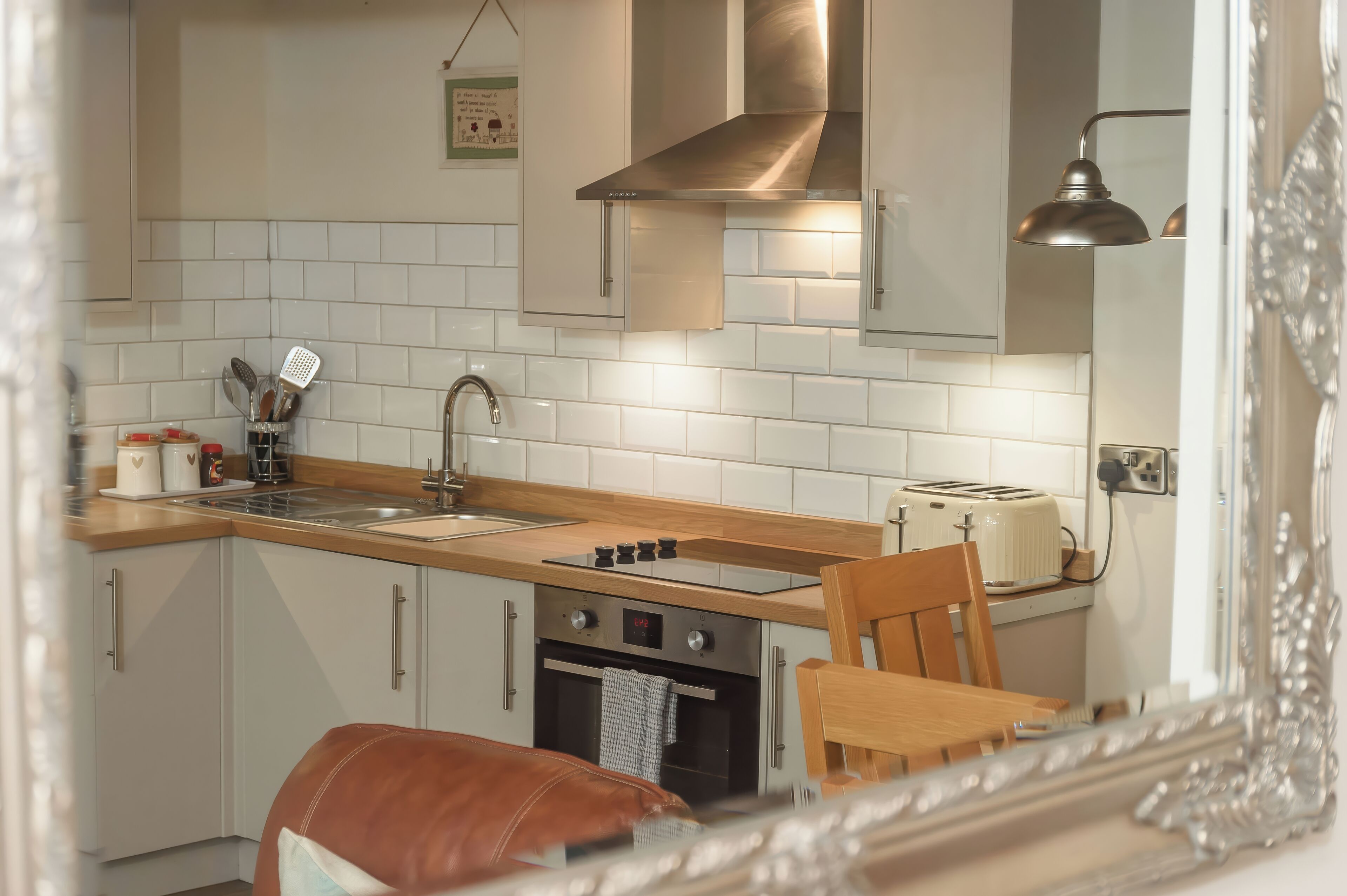 A kitchen with white cabinets, a wooden countertop, a stainless steel range hood, a toaster, and a sink.