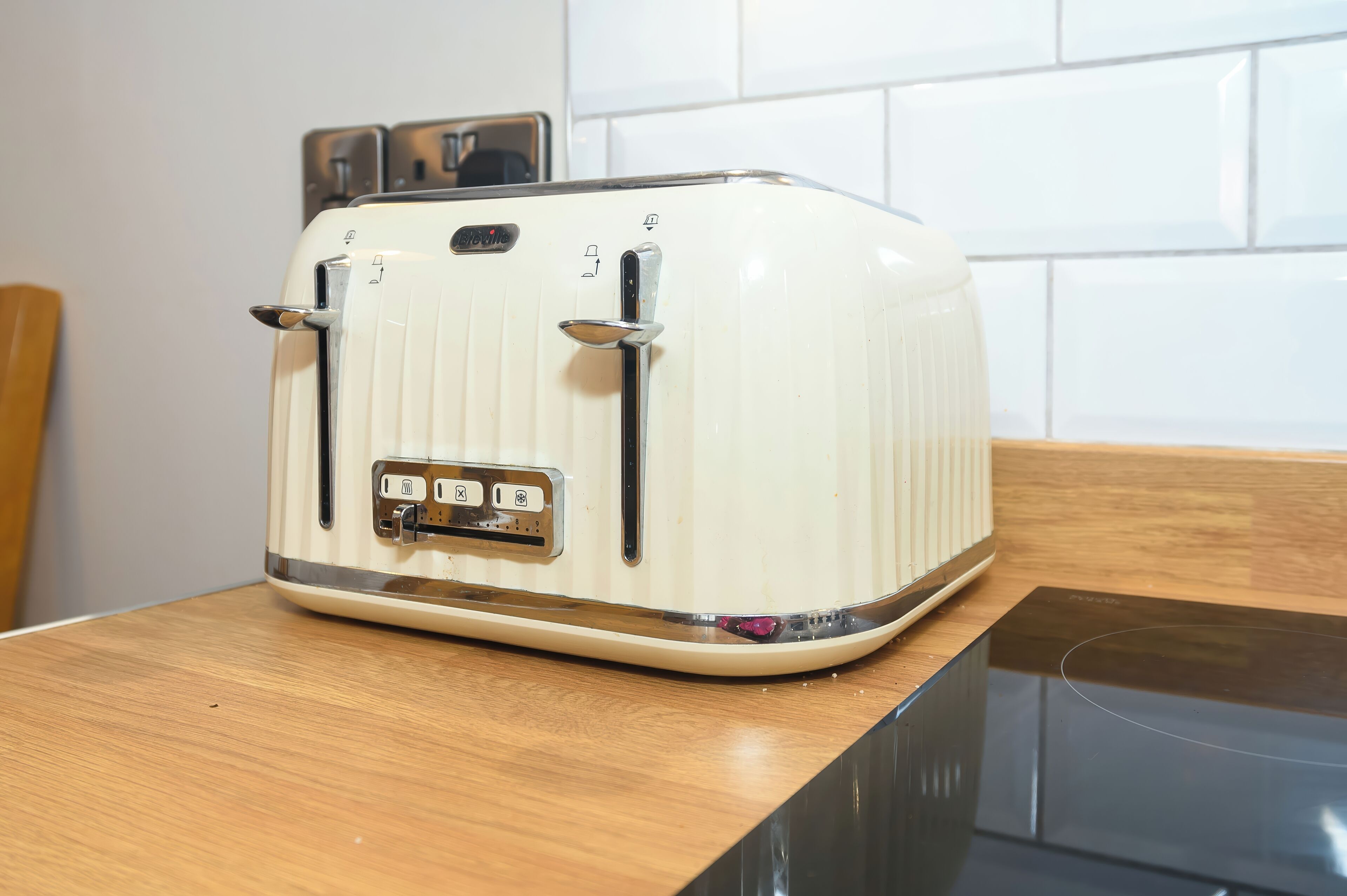 Un tostador blanco antiguo sobre una encimera de madera con una cocina por inducción moderna debajo.