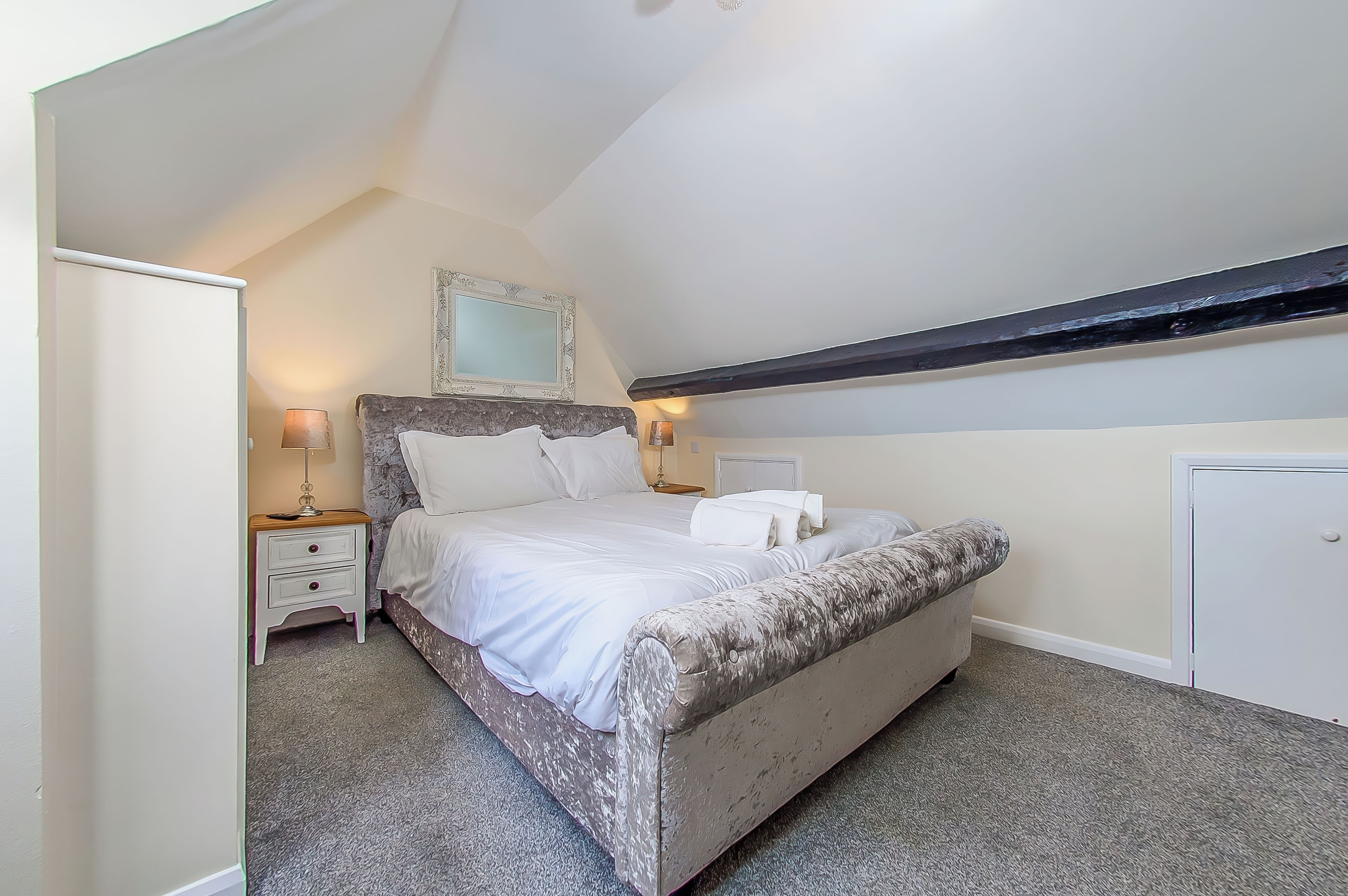 A bedroom with a bed, bedside tables, a mirror, and a wardrobe.