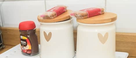 Two white ceramic jars with heart designs, one with a red lid and a jar of Nescafé Original coffee, and a wooden cutting board on top of the jars.