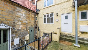 A narrow alleyway between two buildings with a stone wall on the left and a yellow building on the right. - 5 Ivy Yard (Whitby)