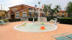 Ett område med vattenlek, bestående av en rund pool, solstolar och en byggnad i bakgrunden.