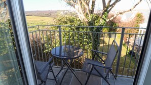 Un balcó amb una taula i dues cadires, amb vista a un jardí amb una palmera i paisatge rural.