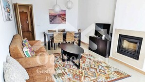 Una sala de estar con un sofá marrón, un tapiz estampado, una mesa de comedor con sillas, una chimenea y un cuadro en la pared.