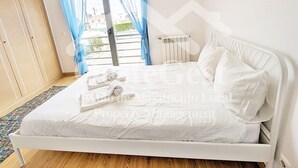 A bedroom with a bed, blue curtains, a radiator, and artwork on the wall.