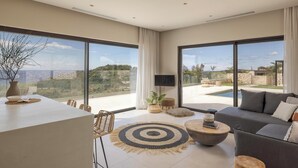 Una sala de estar moderna con un ventanal grande, un sofá, una mesa de centro y un comedor con sillas.