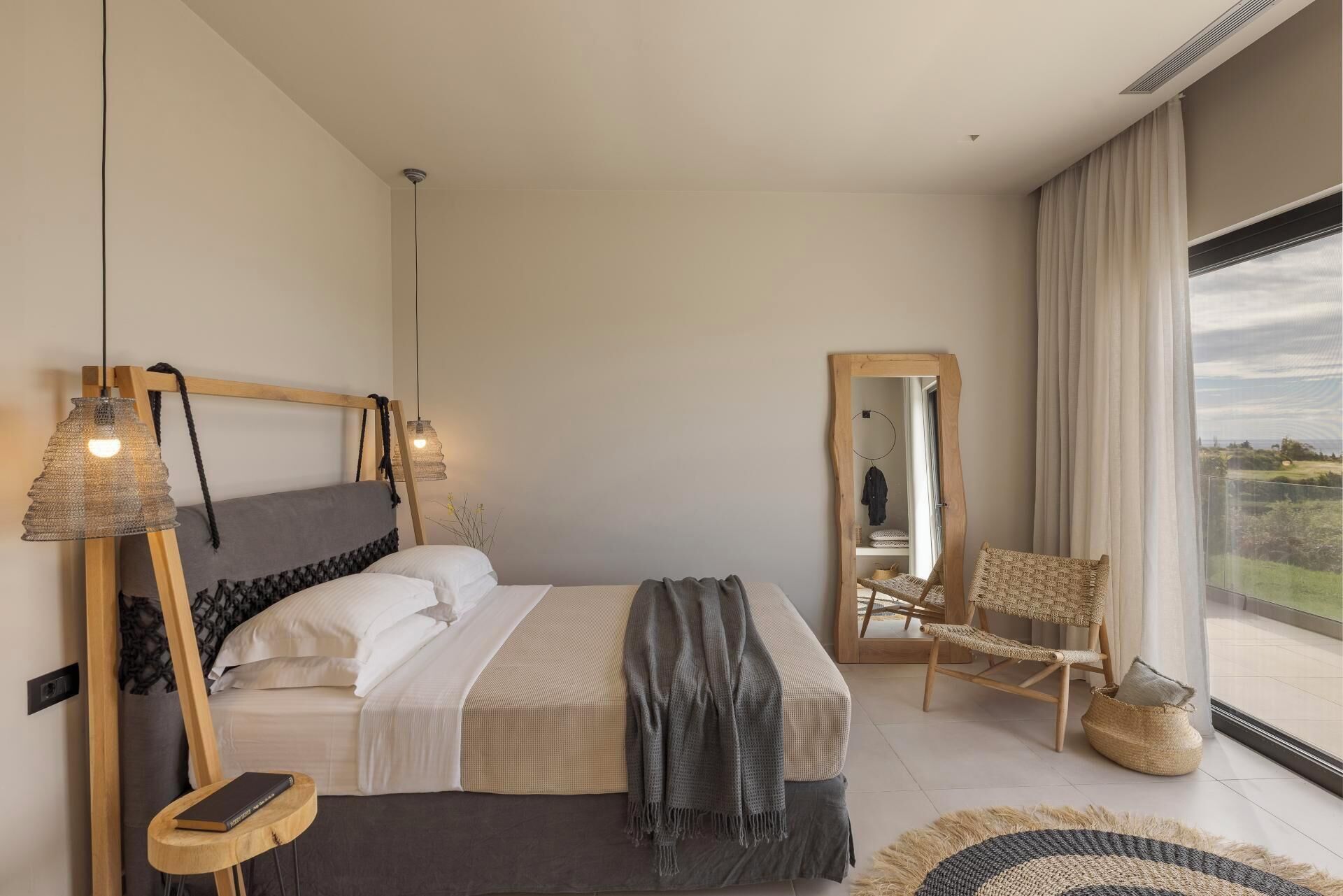 Une chambre à coucher moderne avec un grand lit, des lampes de chevet, un fauteuil et une vue sur l’extérieur.