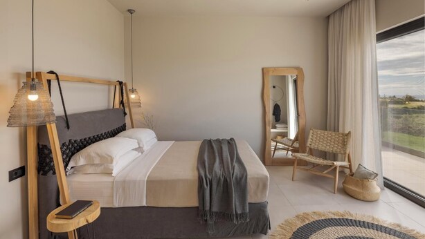 Un dormitorio moderno con una cama grande, lámparas de noche, una silla y vistas al exterior.