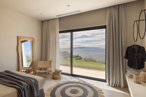 A bedroom with a large sliding glass door leading to a balcony with a view of the sea.