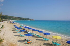 Una spiaggia con file di lettini e ombrelloni, un mare cristallino e un paesaggio collinare sullo sfondo.