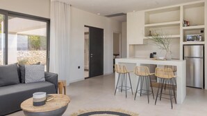 Un espacio habitable moderno con sofá, mesa de centro y área de cocina que incluye refrigerador, taburetes de bar y microondas.