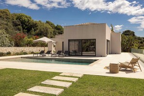 Una casa moderna con piscina, mobiliario exterior y un muro de piedra.