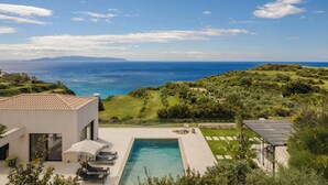 Una villa moderna con piscina, mobiliario exterior y vistas al mar.