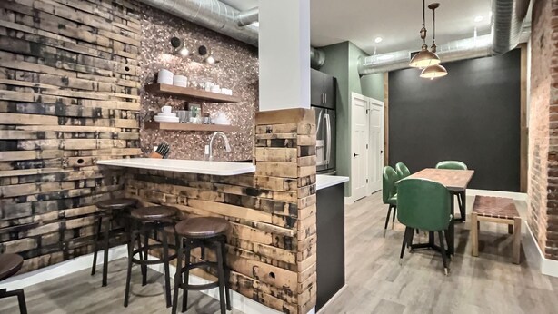 A modern kitchen with a brick accent wall, a central island with stools, and a dining area with green chairs.