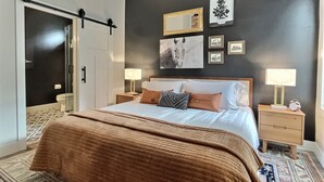 A bedroom with a bed, two bedside tables, a nightstand, a mirror, and wall art.