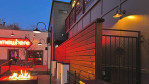An outdoor seating area with a fire feature, a metal gate, and a building with a neon sign.