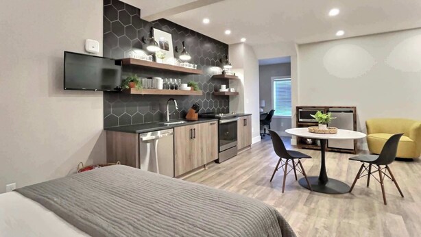 Et moderne køkken med indbyggede hårde hvidevarer, et spiseområde med et rundt bord og stole, samt en separat opholdsstue med en sofa.