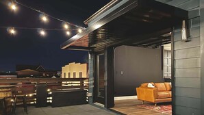 Une terrasse ouverte avec un canapé, un coin repas avec des chaises et des guirlandes lumineuses.