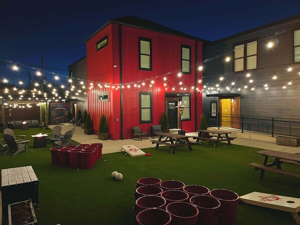 A red building with outdoor seating, string lights, and a green lawn.
