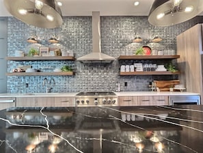 A modern kitchen with a central island, pendant lighting, and a textured backsplash.