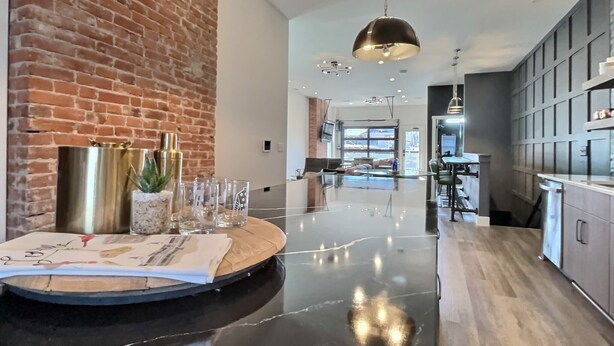 Une cuisine moderne avec un plan de travail en marbre, un mur en briques et un luminaire suspendu.