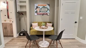 Un pequeño comedor con una mesa redonda y dos sillas, un sofá y un letrero en la pared.