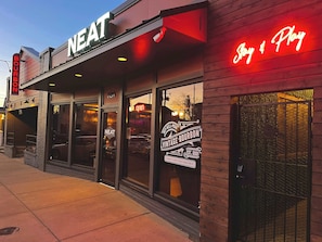 Un bâtiment orné d’une enseigne au néon indiquant les mots « NEAT » et « Bourbon », ainsi que d’une autre enseigne au néon avec les mots « Joy & Play ».