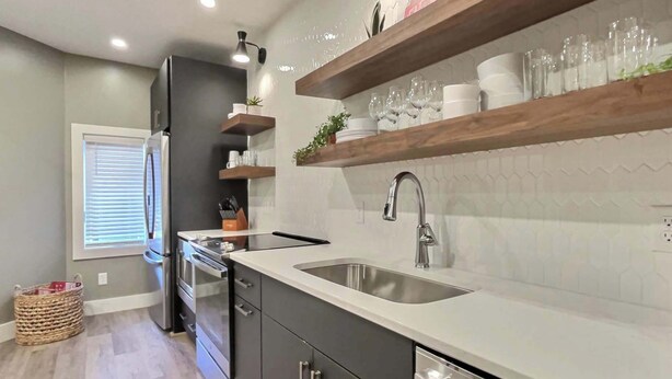 Una cocina moderna con un lavamanos de acero inoxidable, estantes de madera y un horno empotrado.