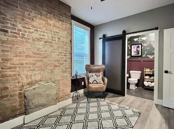 Una habitación con paredes de ladrillo visto, una puerta corredera que da al baño y una alfombra estampada.
