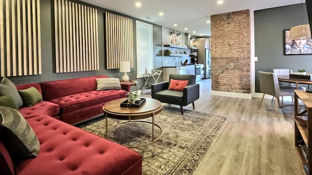 A modern living room with a red sofa, a round coffee table, and a kitchen in the background. - Swanky & Upbeat Suites @ Bungalou + Bourbon Bar (Louisville)