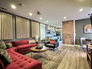 Una sala moderna con un sofá rojo, una mesa de centro redonda y una cocina al fondo.