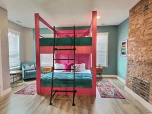 A bunk bed room with a ladder, two bedside tables, a chair, and a brick wall. - Swanky & Upbeat Suites @ Bungalou + Bourbon Bar (Louisville)