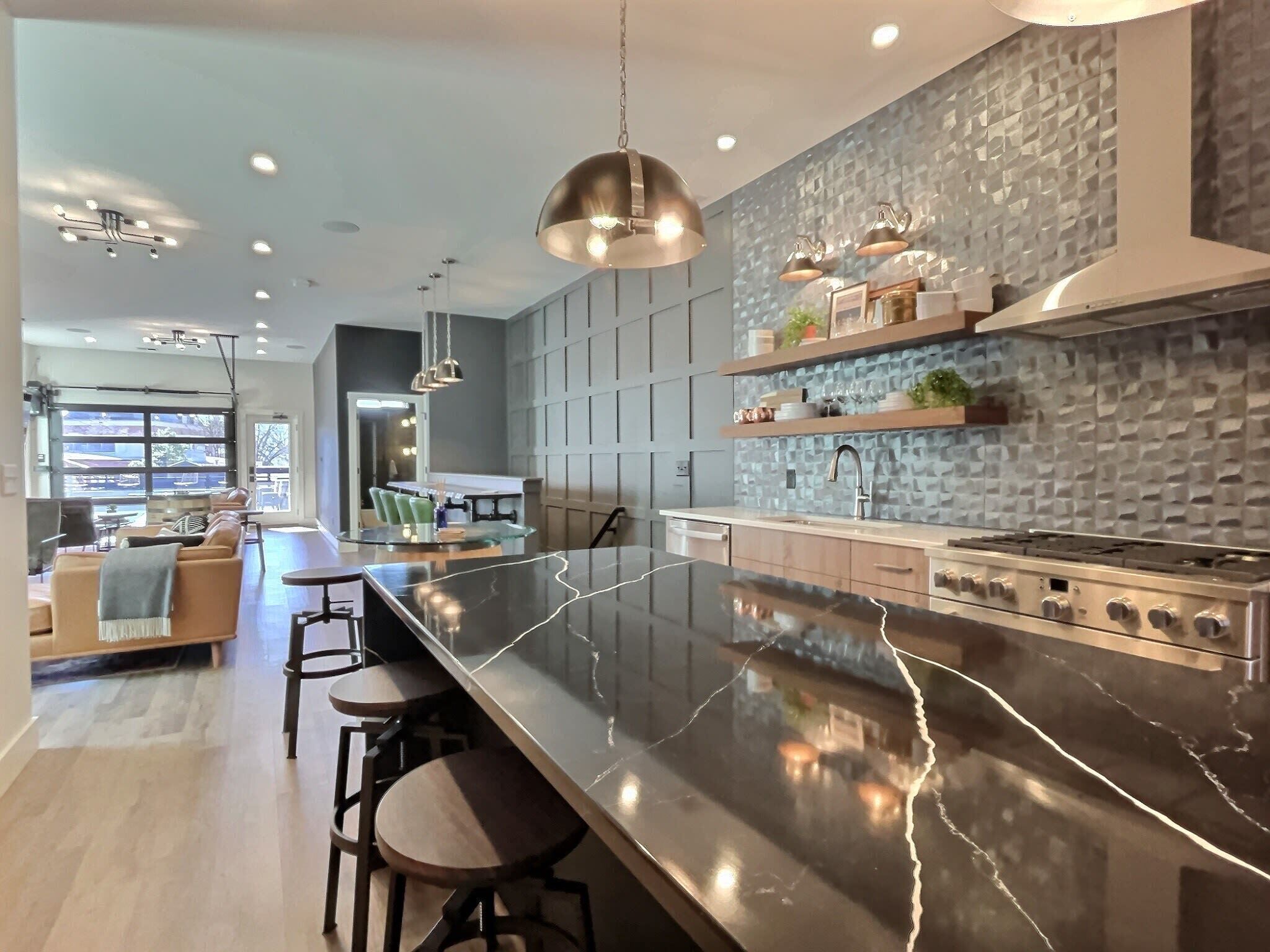 Una cucina moderna con un'isola grande, illuminazione a sospensione e una parete di fondo decorata.