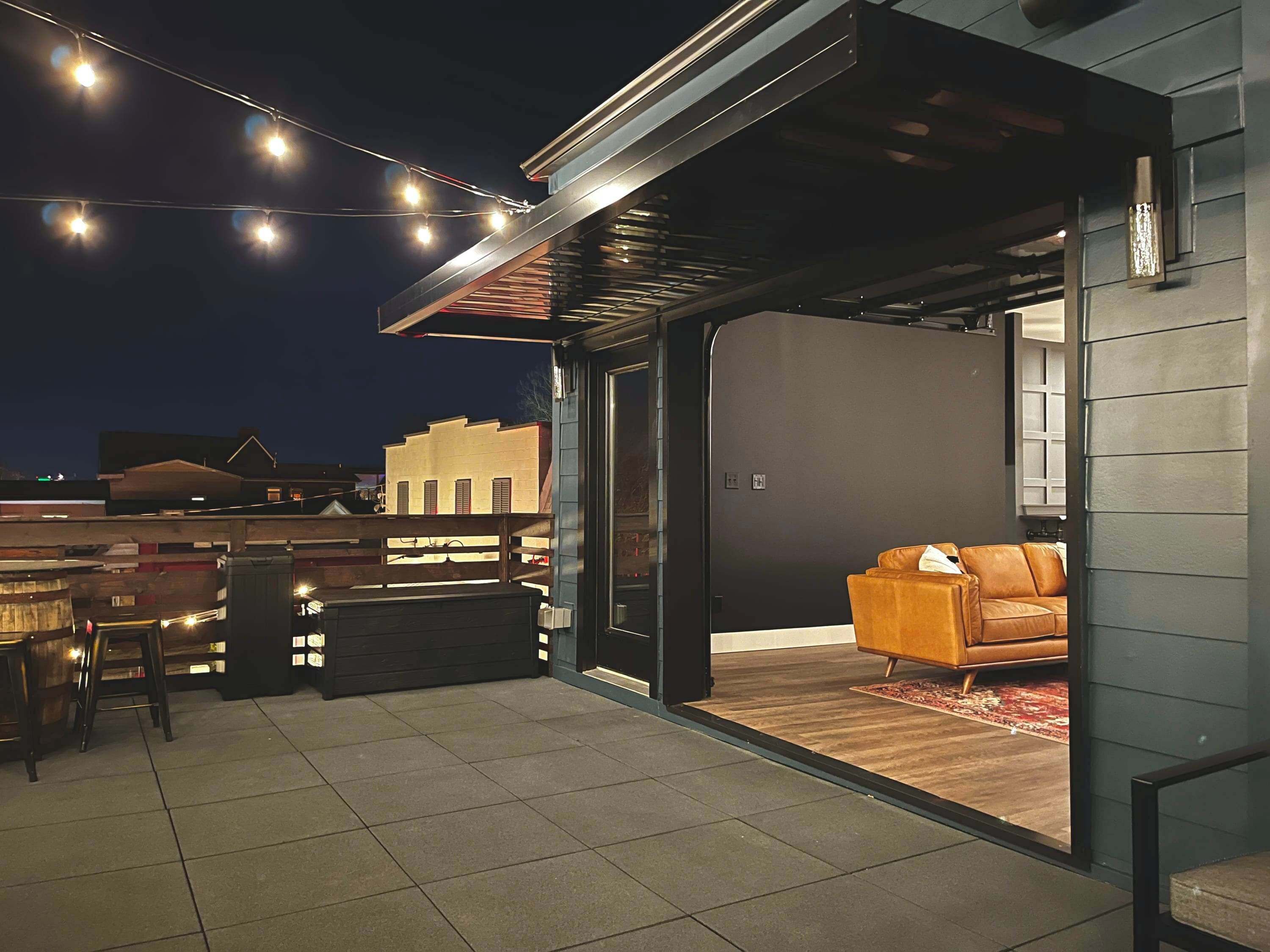 Une terrasse ouverte avec un canapé, un coin repas avec des chaises et des guirlandes lumineuses.