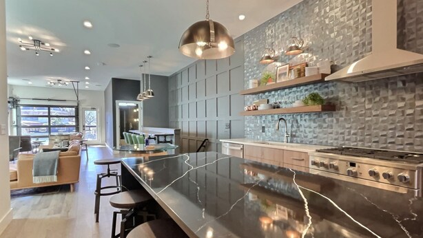 A modern kitchen with a large island, pendant lighting, and a textured backsplash.