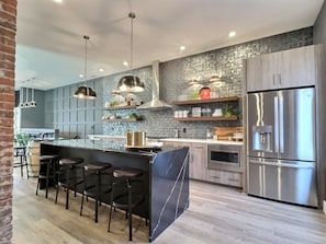 Una cocina moderna con una isla central, taburetes de bar, electrodomésticos de acero inoxidable y una pared de ladrillo.