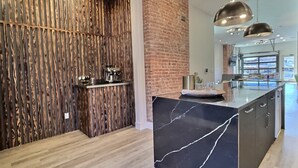 A modern kitchen with a marble island, a brick accent wall, and a wooden vertical panel.