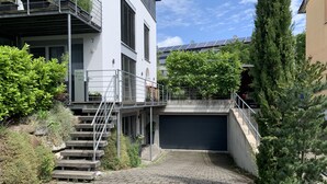 A modern building with a staircase leading to a garage, surrounded by greenery and a clear sky.
