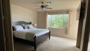 Une chambre à coucher avec un lit, un ventilateur de plafond, une fenêtre avec des rideaux et un sol recouvert de moquette.