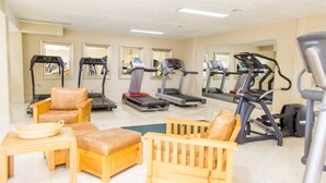Une salle de sport équipée de tapis de course, de vélos d’appartement et d’un petit espace détente avec une table et des chaises.