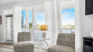 Una habitación con dos sillones estampados, una mesita de cristal con una lámpara y vistas a un balcón con barandilla.