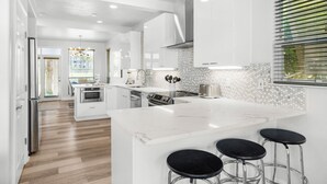 Una cocina moderna con armarios blancos, una isla de mármol y taburetes negros.