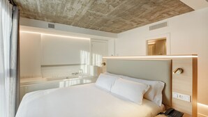 A modern hotel room with a large bed, a bedside table with a phone, a mirror, and a bathroom with a sink and shower. - Sercotel Granada Suites (Granada)