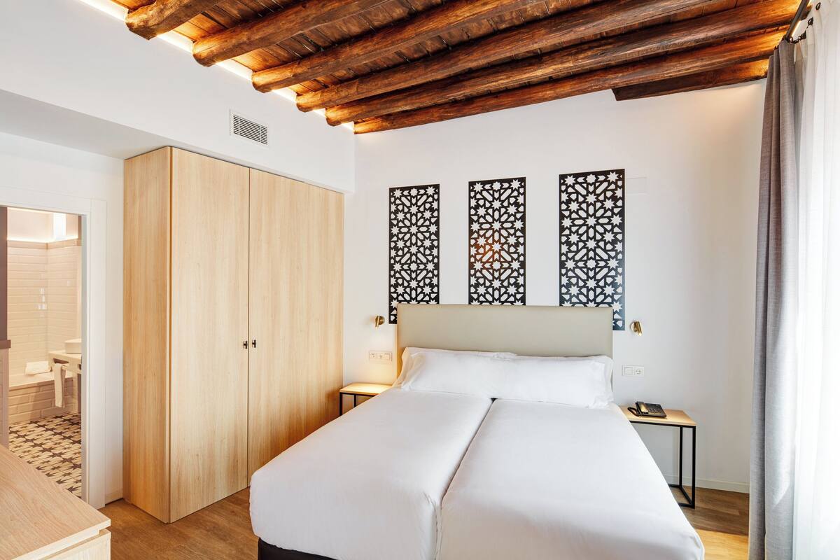 A hotel room with a wooden ceiling, a large bed, a wardrobe, and decorative wall panels.