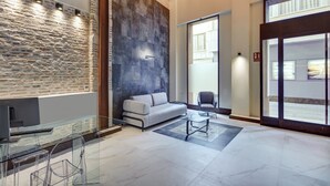 Un vestíbulo moderno con pared de piedra, un sofá gris, una mesa de vidrio y una silla.