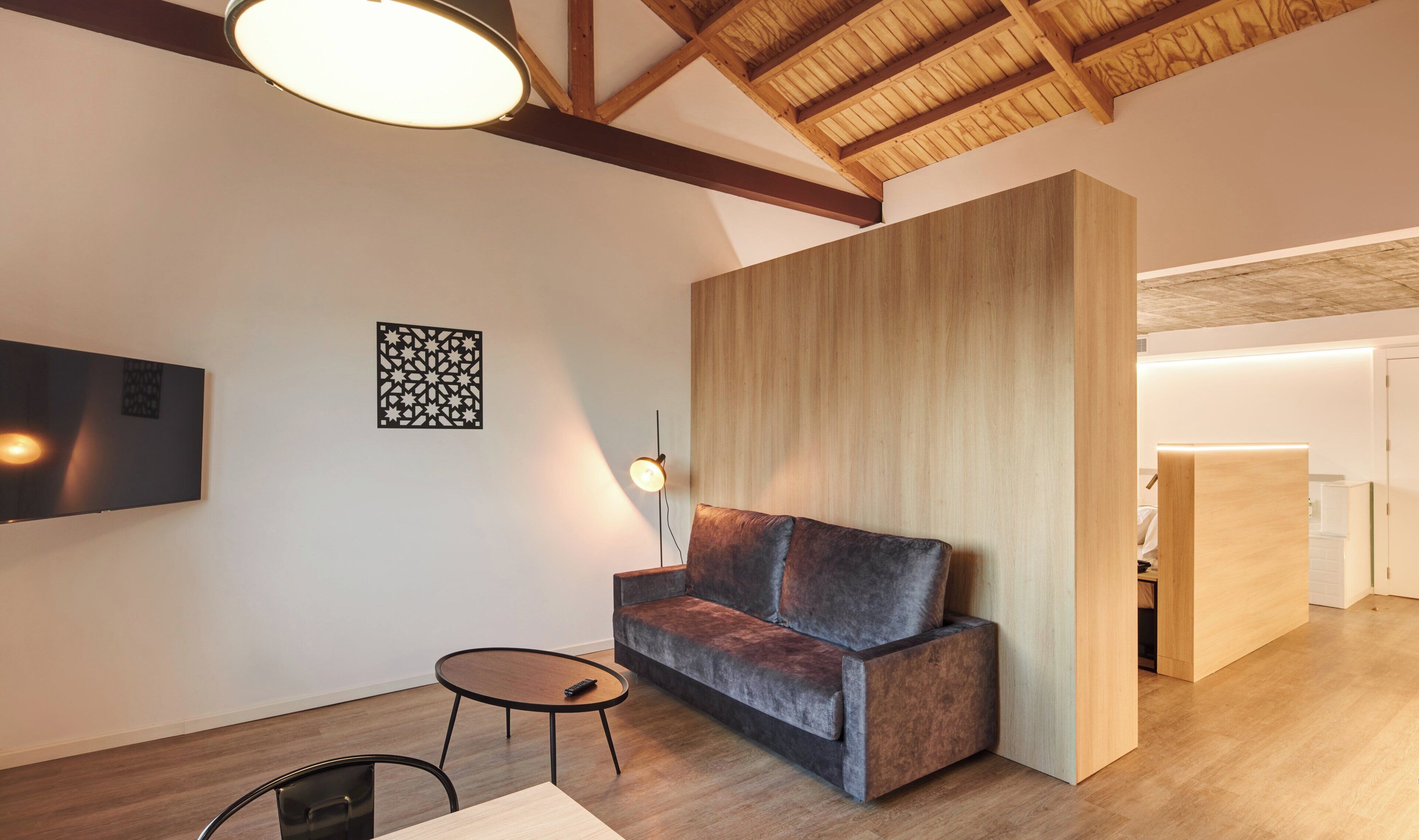 Un salon moderne avec un canapé gris foncé, une petite table ronde et un téléviseur fixé au mur.