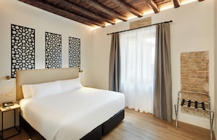 A hotel room with a large bed, a nightstand, a telephone, and a decorative wall panel.