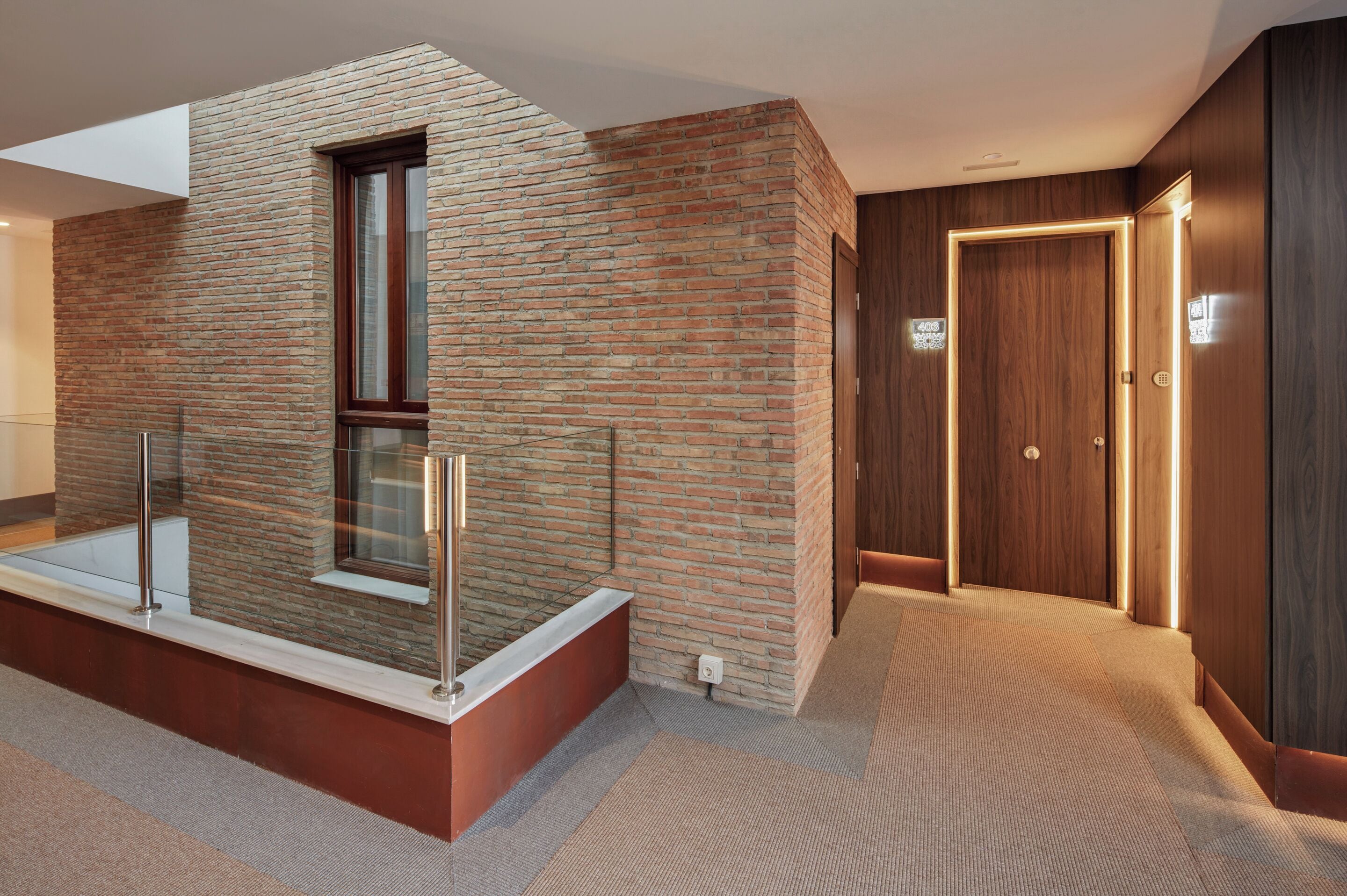 A modern bathroom with a glass-enclosed bathtub, a brick wall, and a wooden door.