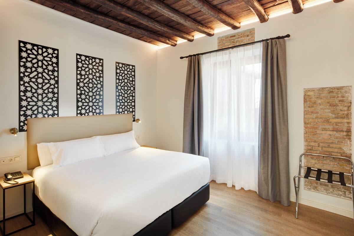 A hotel room with a large bed, a nightstand, a chair, and decorative wall panels.